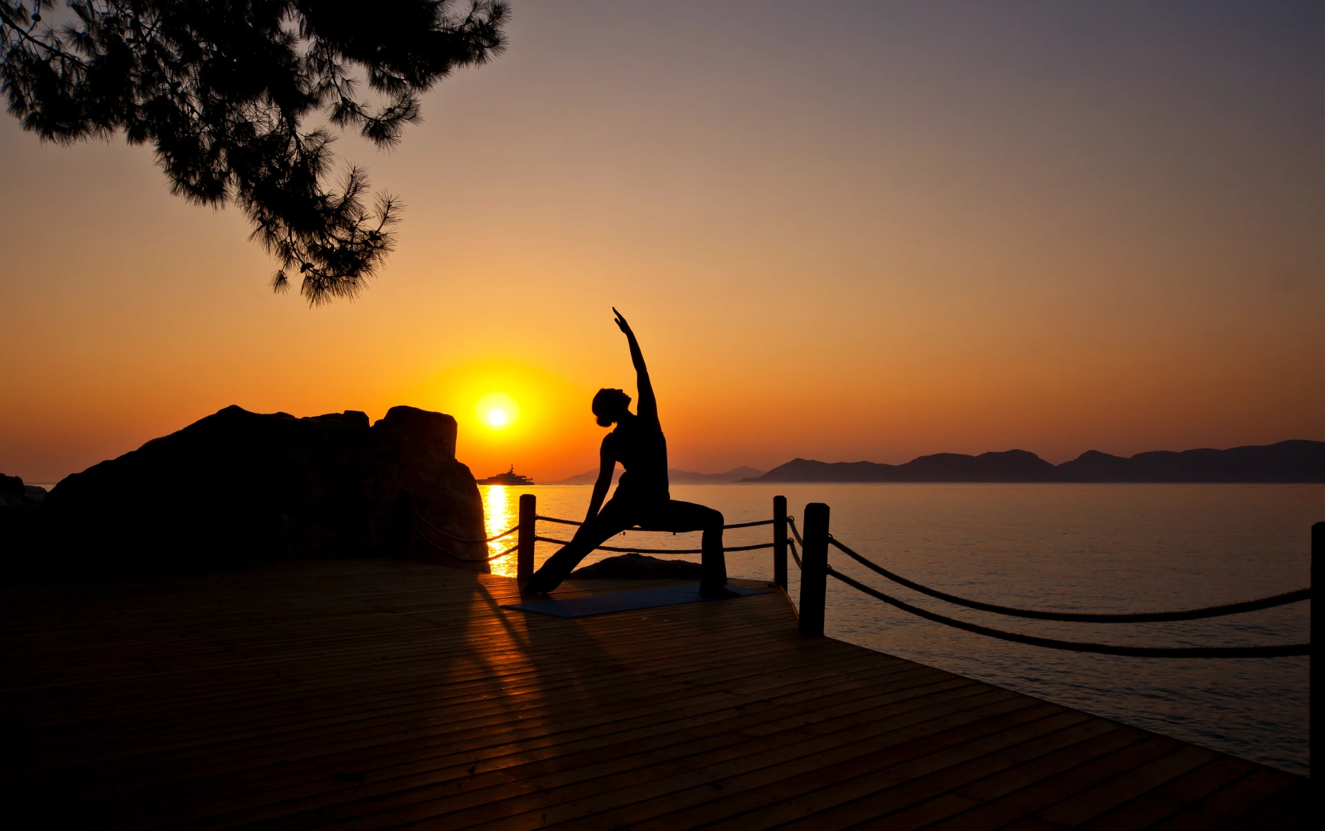 Güneş tepelerin ardına inerken deniz kıyısındaki terasta yoga